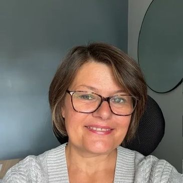 Smiling woman with glasses and short hair in a cozy white sweater.
