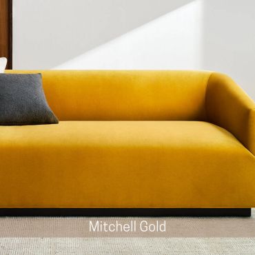 Mustard yellow sofa with a dark gray pillow against a white wall.
