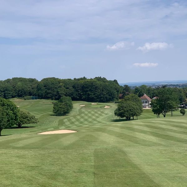 A scenic golf course with sand bunkers and striped fairways under a blue sky.