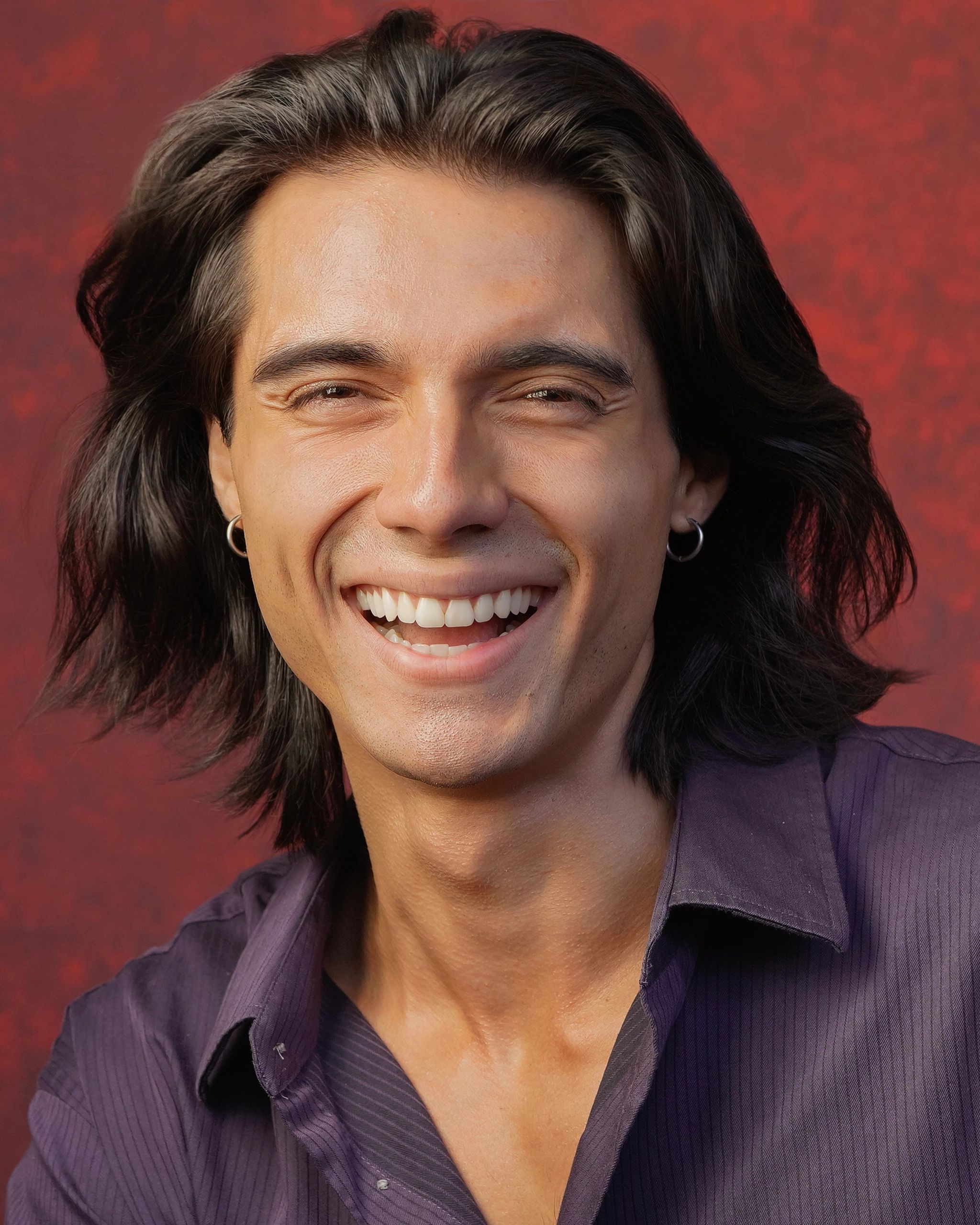 Smiling young man with long hair wearing a purple shirt.