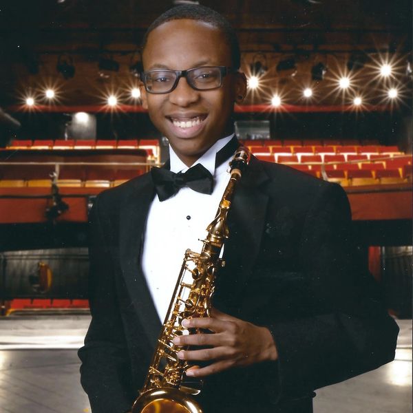 Young man in tuxedo holding a saxophone on stage.