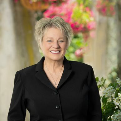 Smiling woman in black blazer with floral background.