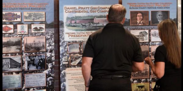 Two people view historic preservation panels about cotton gin companies.