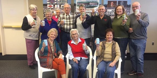 Group of seniors holding mugs, smiling indoors.