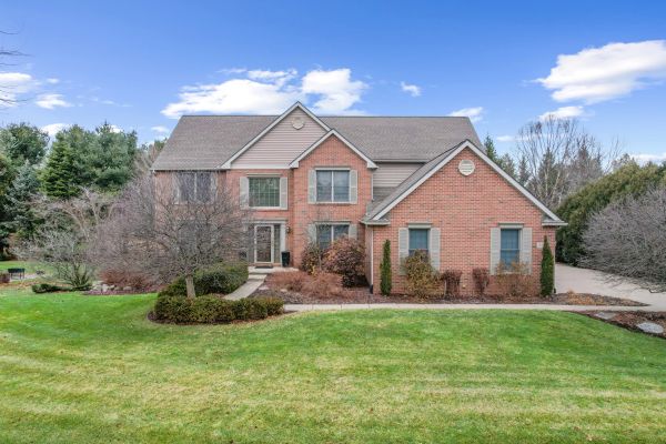 Large two-story brick and siding house with a spacious lawn under a blue sky.