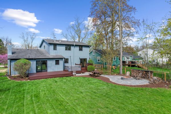 Spacious backyard with wooden deck, fire pit, and green lawn.