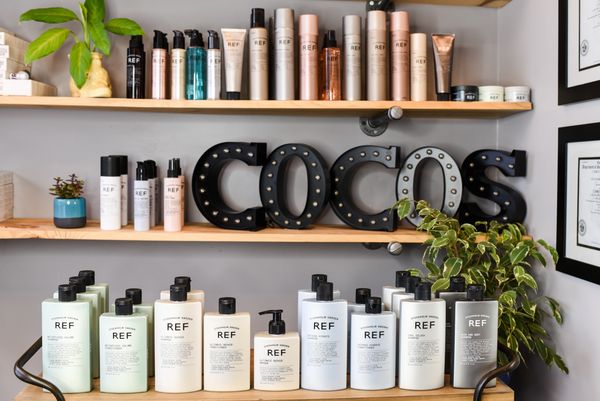 REF hair care products displayed on wooden shelves with decorative plants and COCO'S sign.