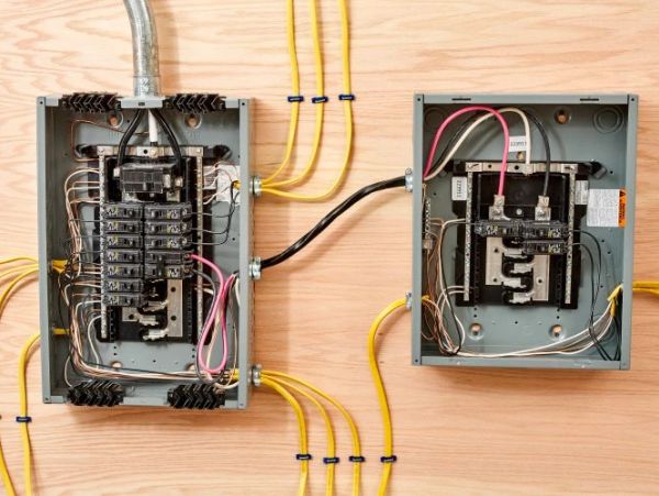 Two open electrical breaker panels with connected yellow wires on wood.