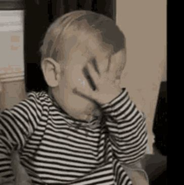 A baby covering face with hand in a striped shirt.