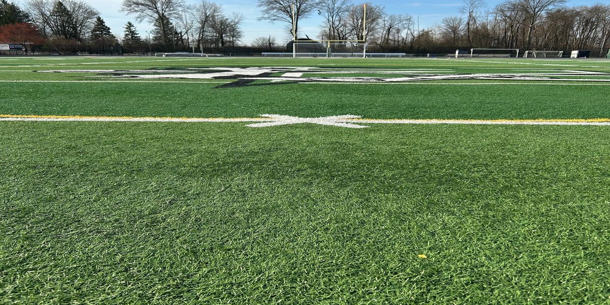 Empty football field with goalposts and trees in the background.