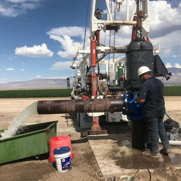 Worker in helmet operating irrigation equipment on a farm under blue sky.