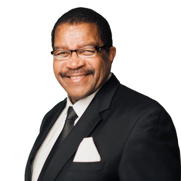 Smiling man in a black suit and glasses against a white background.