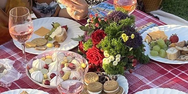 A picnic with snacks, wine, flowers, and people holding playing cards.