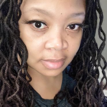 Close-up of a woman with long dreadlocks and expressive eyes.
