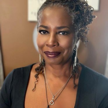 Confident woman with braided hair and elegant jewelry smiling.
