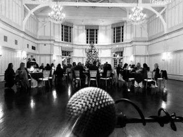 Microphone view facing an audience in a festive event hall with a decorated Christmas tree.