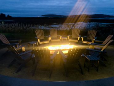 A cozy nighttime fire pit surrounded by empty wooden chairs.