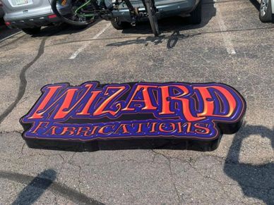 Colorful sign on pavement reading 'Wizard Fabrications'.