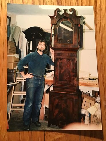 Man in workshop with a tall antique wooden clock.
