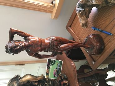 Wooden sculpture of a man standing with one hand on his head.