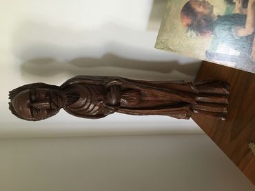 Wooden statue of a bearded man holding an object, placed on a wooden surface.