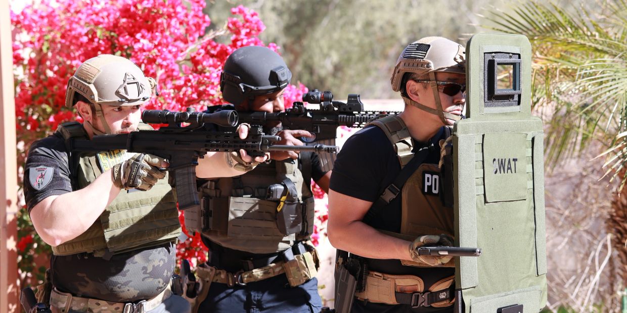 SWAT team members in tactical gear prepare to breach with weapons and shield.