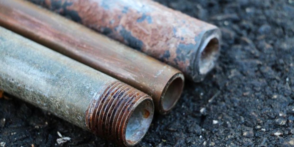 Three rusty metal pipes lying on dark ground.