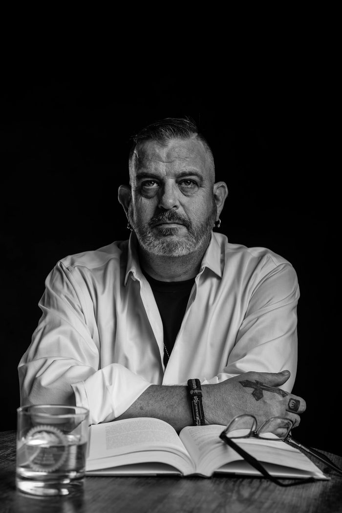 Black and white portrait of a man with a beard and tattoos reading a book.