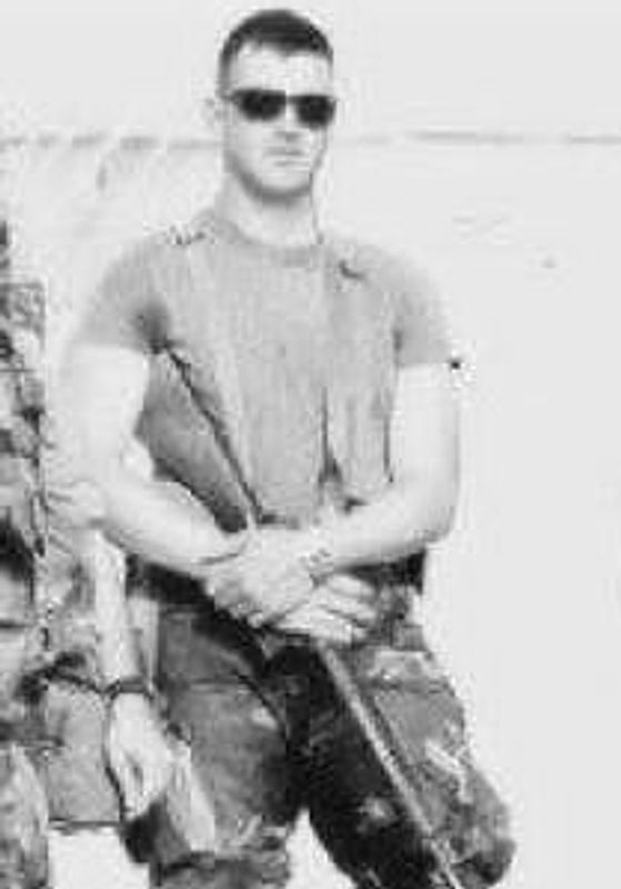 Man in sunglasses holding a rifle, wearing a t-shirt and camouflage pants.