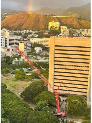 Cityscape with a red crane and a rainbow over a mountain at sunset.