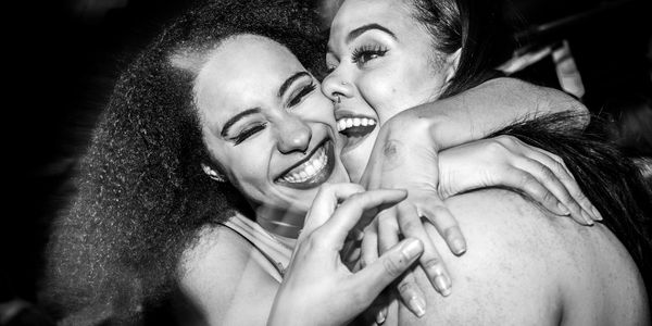Two women joyfully embrace, smiling widely in a candid moment.
