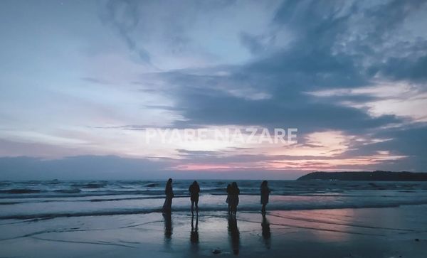 Four people standing on a beach at sunset under a cloudy sky.