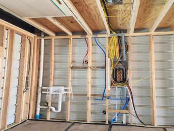 Interior wall framing with plumbing and electrical wiring in progress.