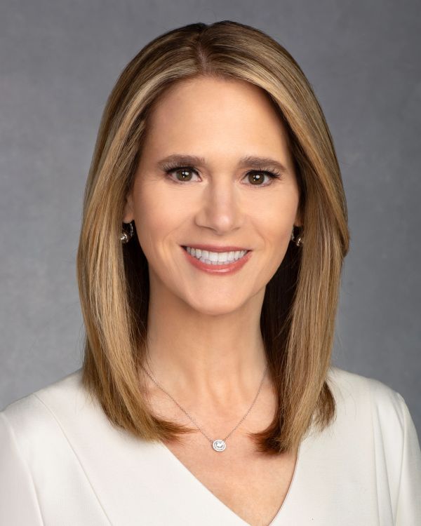 Smiling woman with straight blonde hair in white top against gray background.