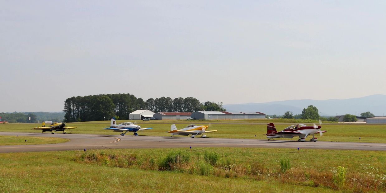 Image showing four planes colored red, yellow & white, blue, and yellow & black taxing down runway.