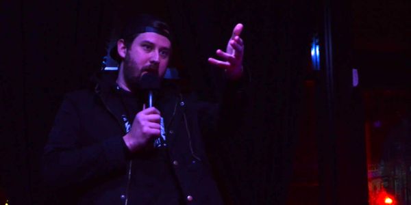 A comedian holding a mic gestures towards the crowd in front of him that we cannot see