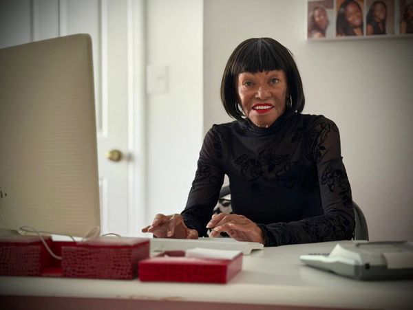 Elderly woman smiling at desk with computer and office items.
