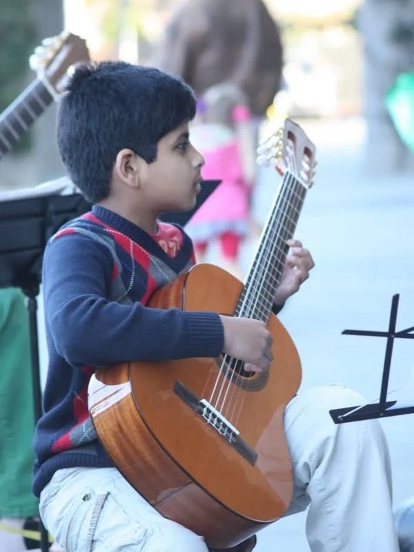 Young boy focused on playing acoustic guitar outdoors.