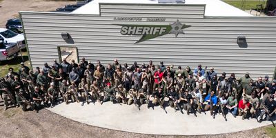 Large group of sheriff deputies posing outside sheriff headquarters.