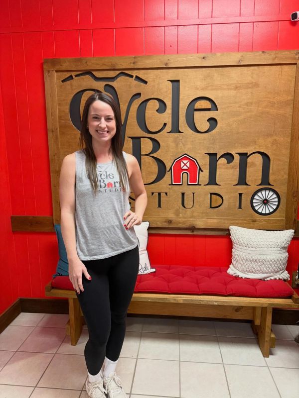 Woman posing in front of Cycle Barn Studio sign with red wall background.