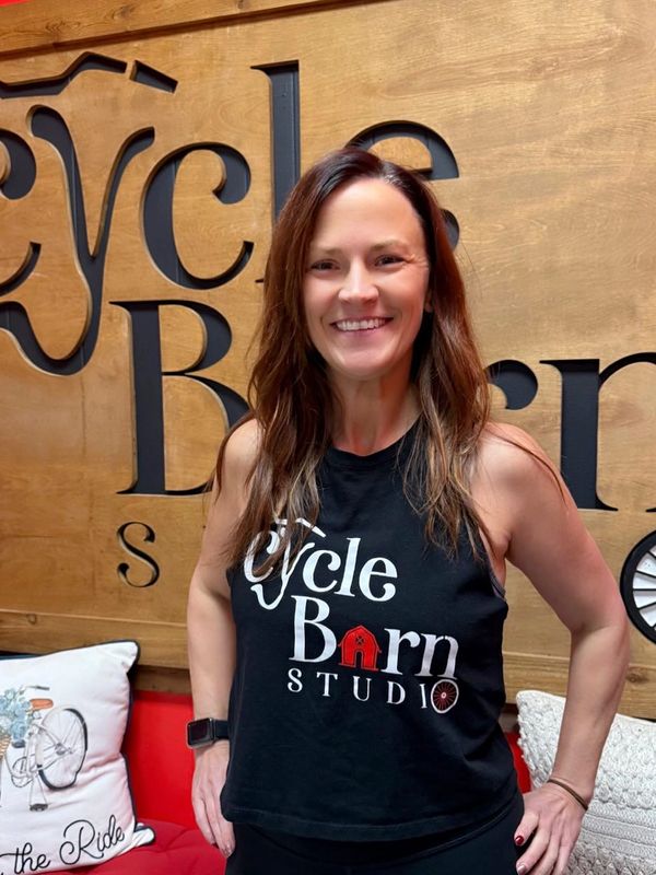 Smiling woman in a Cycle Barn Studio tank top standing indoors.