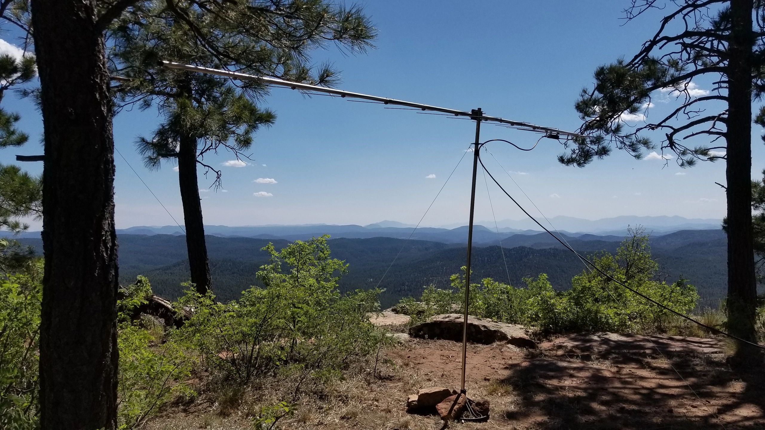 A tall antenna set against a scenic mountainous backdrop under a clear blue sky.