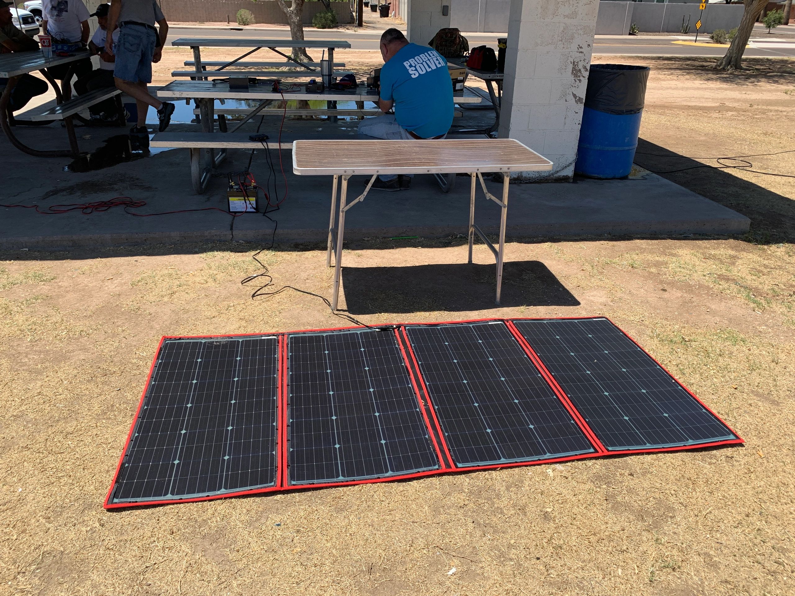 Solar panels set up outdoors near a pavilion with people and equipment.