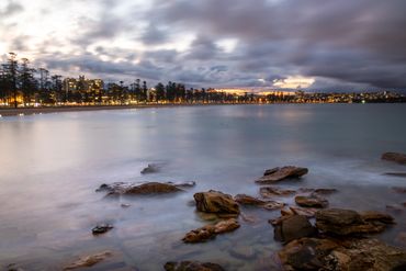 Moody dark, blurred, long exposure clouds over Manly Beach, Sydney, Australia at sunset, city lights