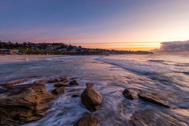 Golden hour photography of Bronte Beach, Sydney, Australia with rocks, waves, dark clouds, and beach