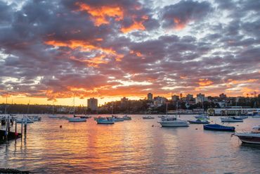 Golden hour photography of Manly Beach Warf, Sydney, Australia with sail boats and vibrant red sky.