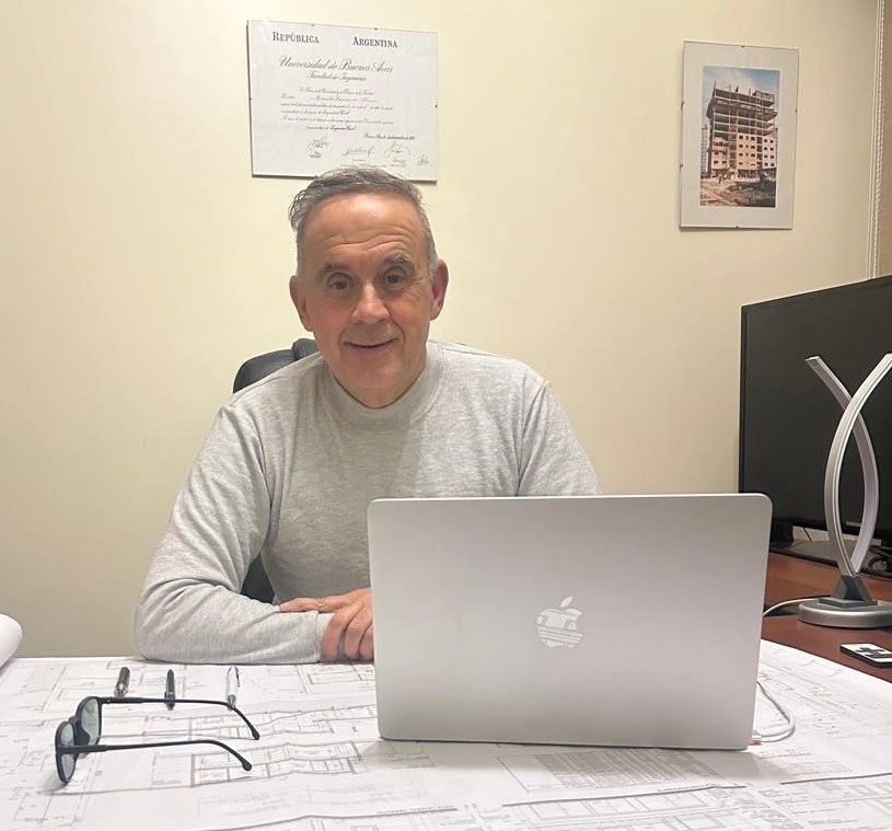 Hombre sentado frente a una laptop en un escritorio con planos.