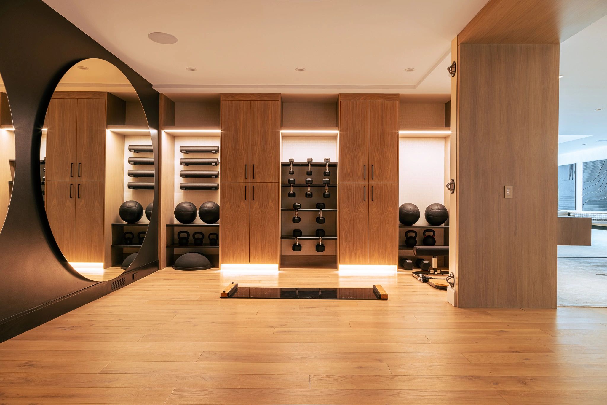 Modern home gym with wooden cabinets, exercise balls, kettlebells, and dumbbells.
