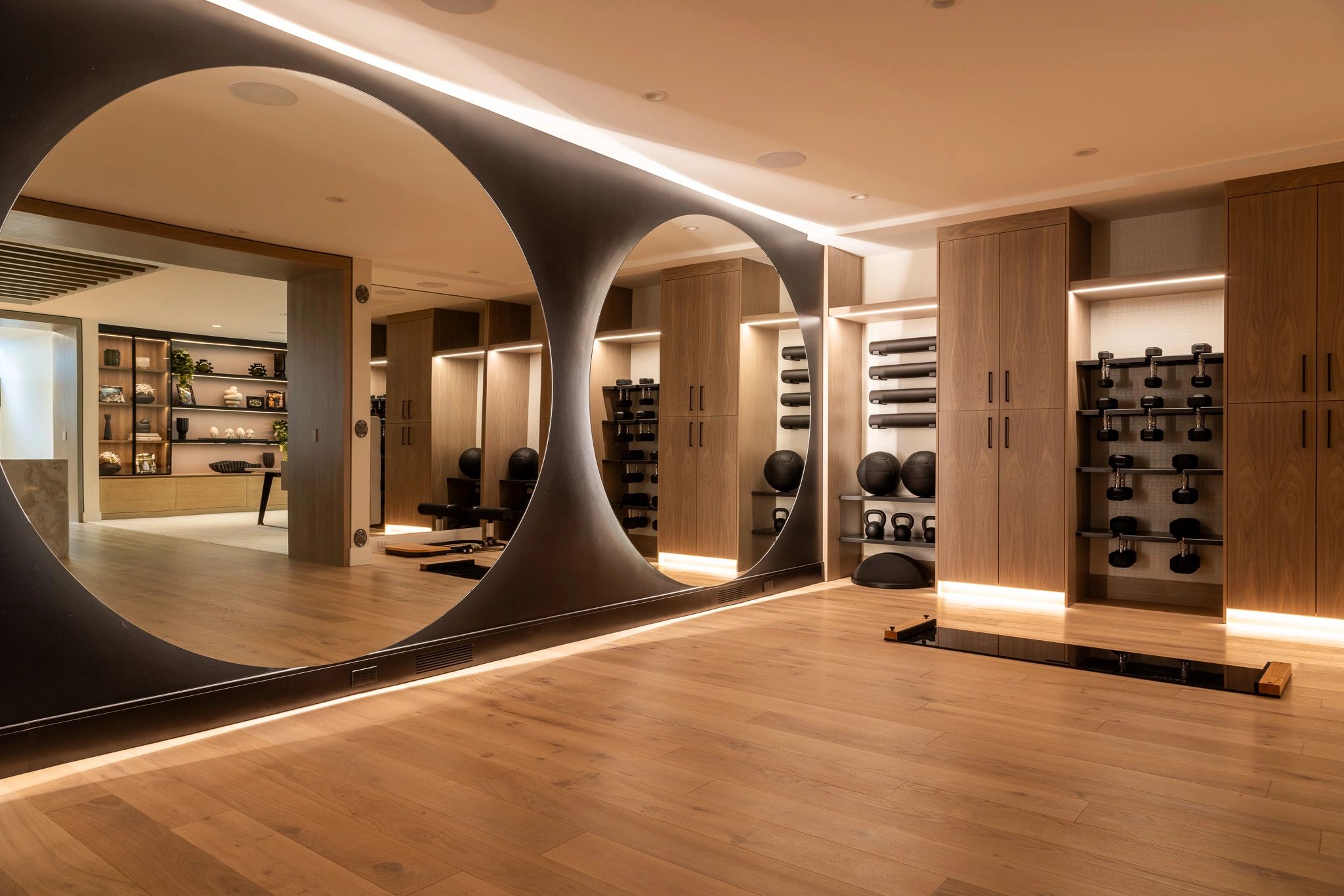 Modern home gym with wooden floors, large circular mirrors, and organized weights.