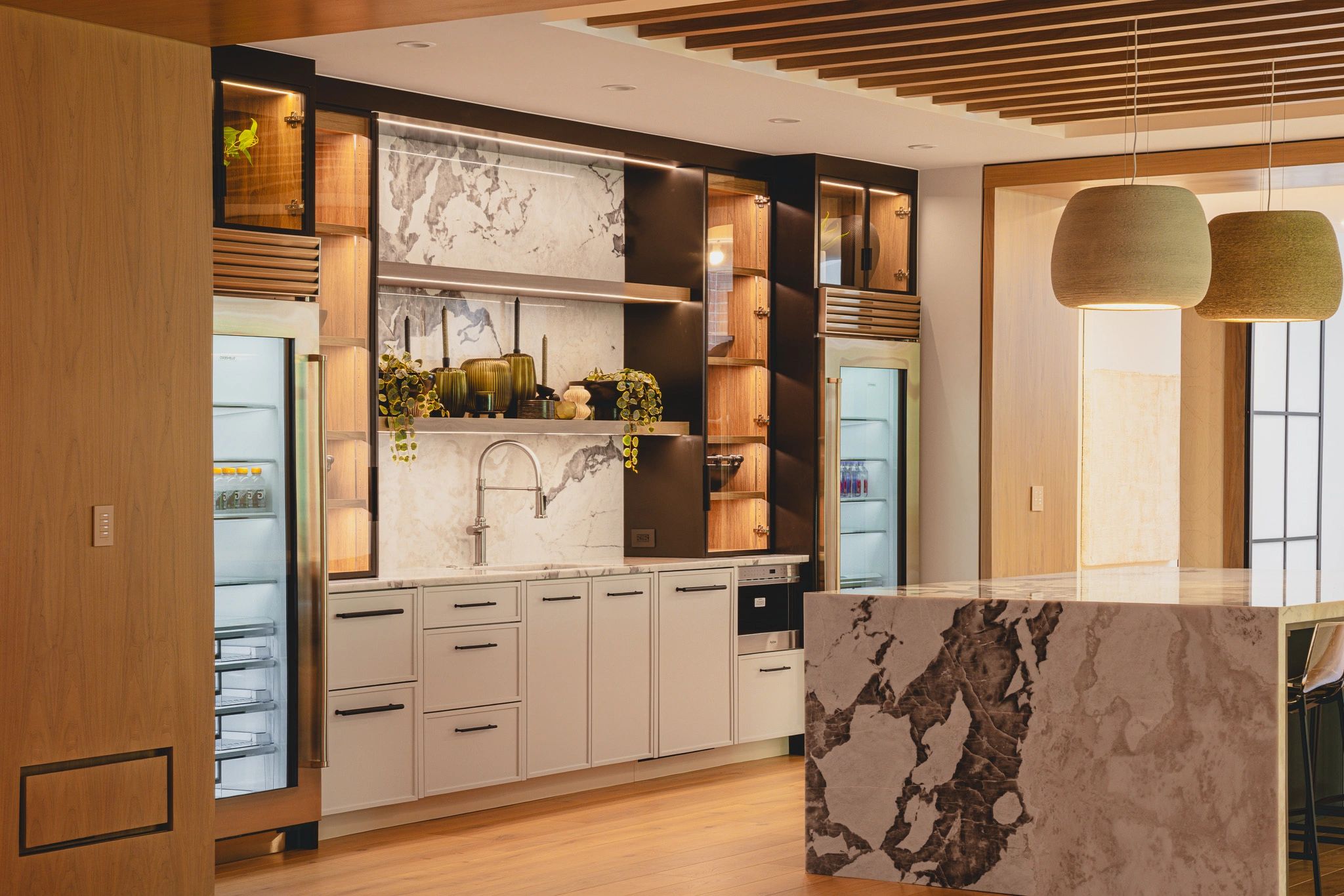 Modern kitchen with marble island, wooden cabinets, and pendant lights.